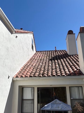 Clay or concrete tile roof planes meeting beside stucco walls and a chimney